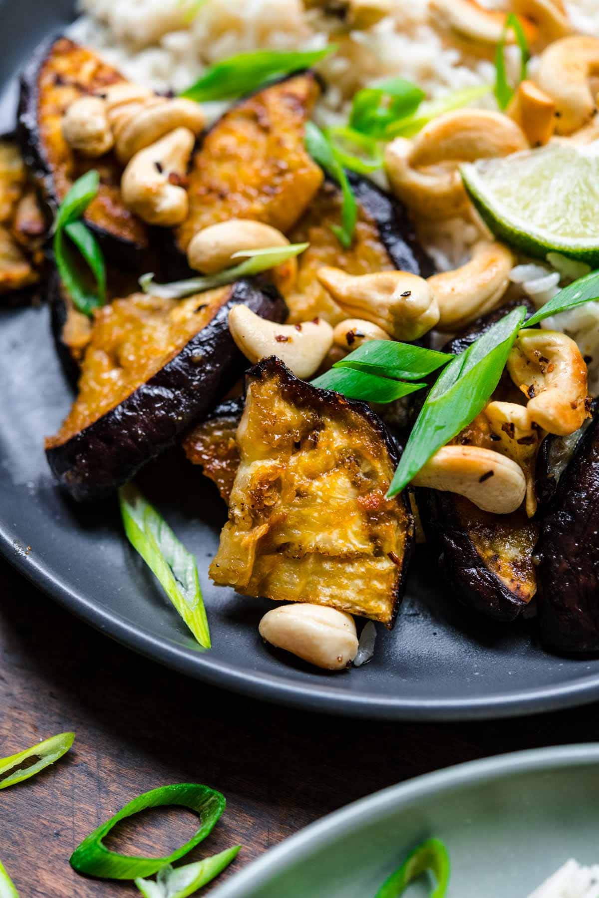 Close up of eggplant on a plate with cashews and green onions.