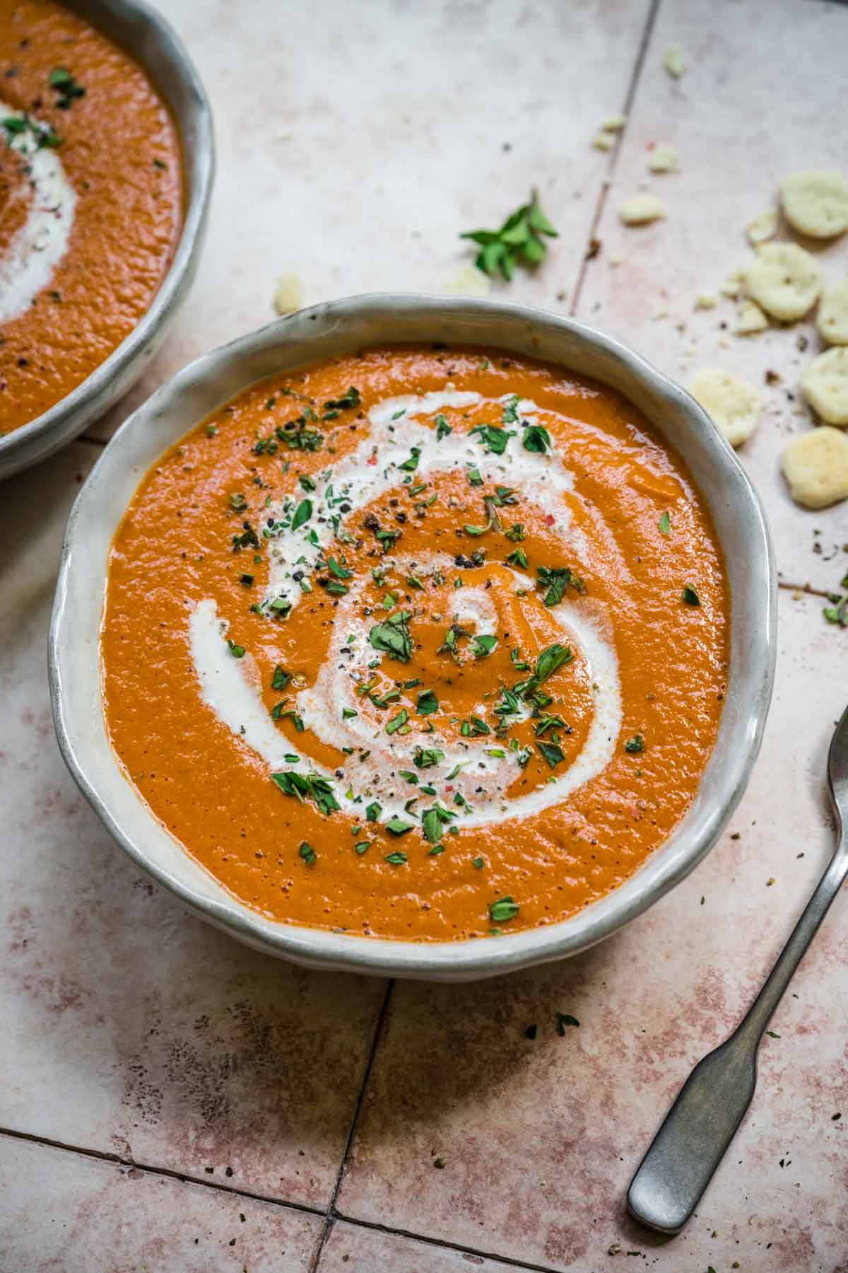 Tomato soup with a swirl of cream in a bowl with a spoon by its side.