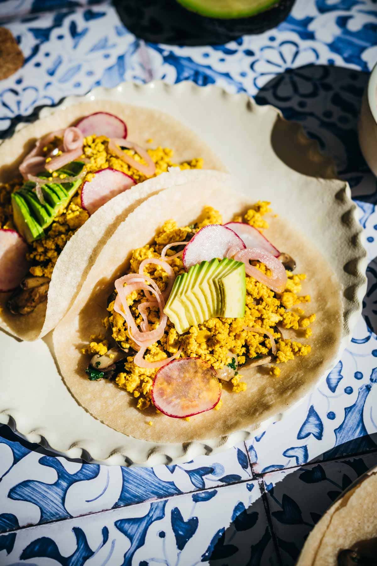 Two tacos on a plate, garnished with onion, radish and avocados.