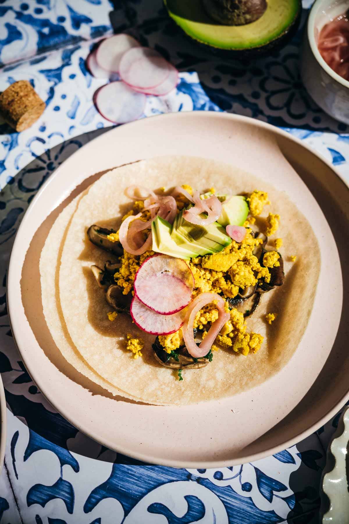 One taco on a plate with tofu, mushrooms, avocado, onions, and radish.