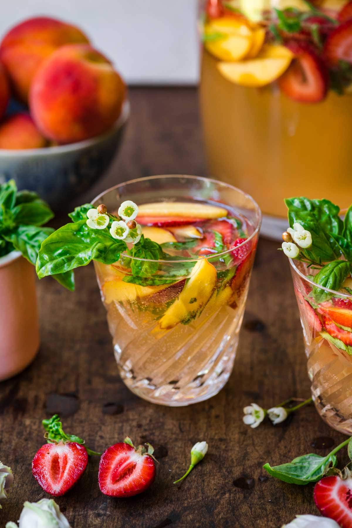 Front view of a glass of sangria with strawberries, peaches, and basil.