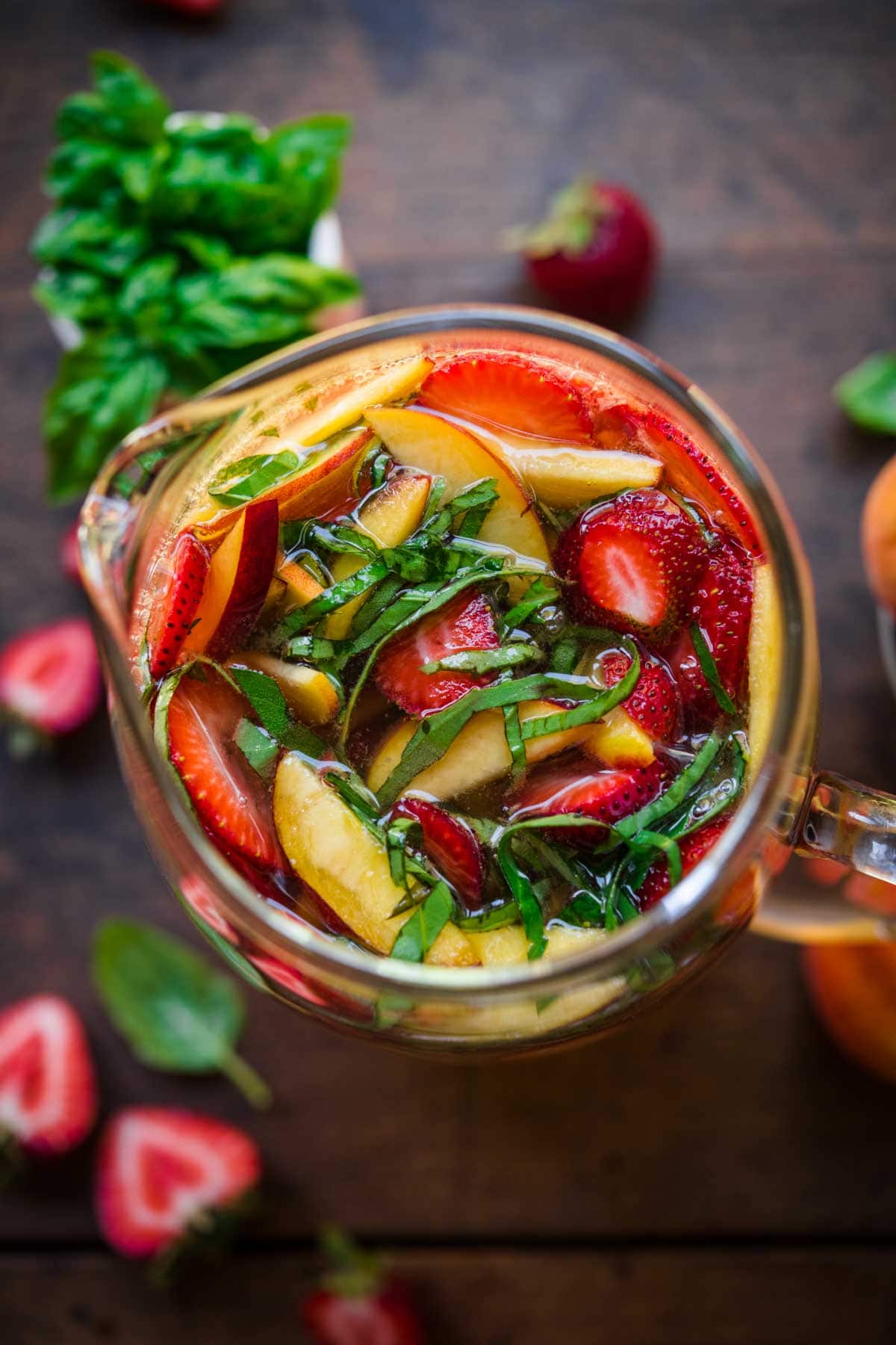 Overhead view of a pitcher of sangria with cut up strawberries, peaches, and basil.