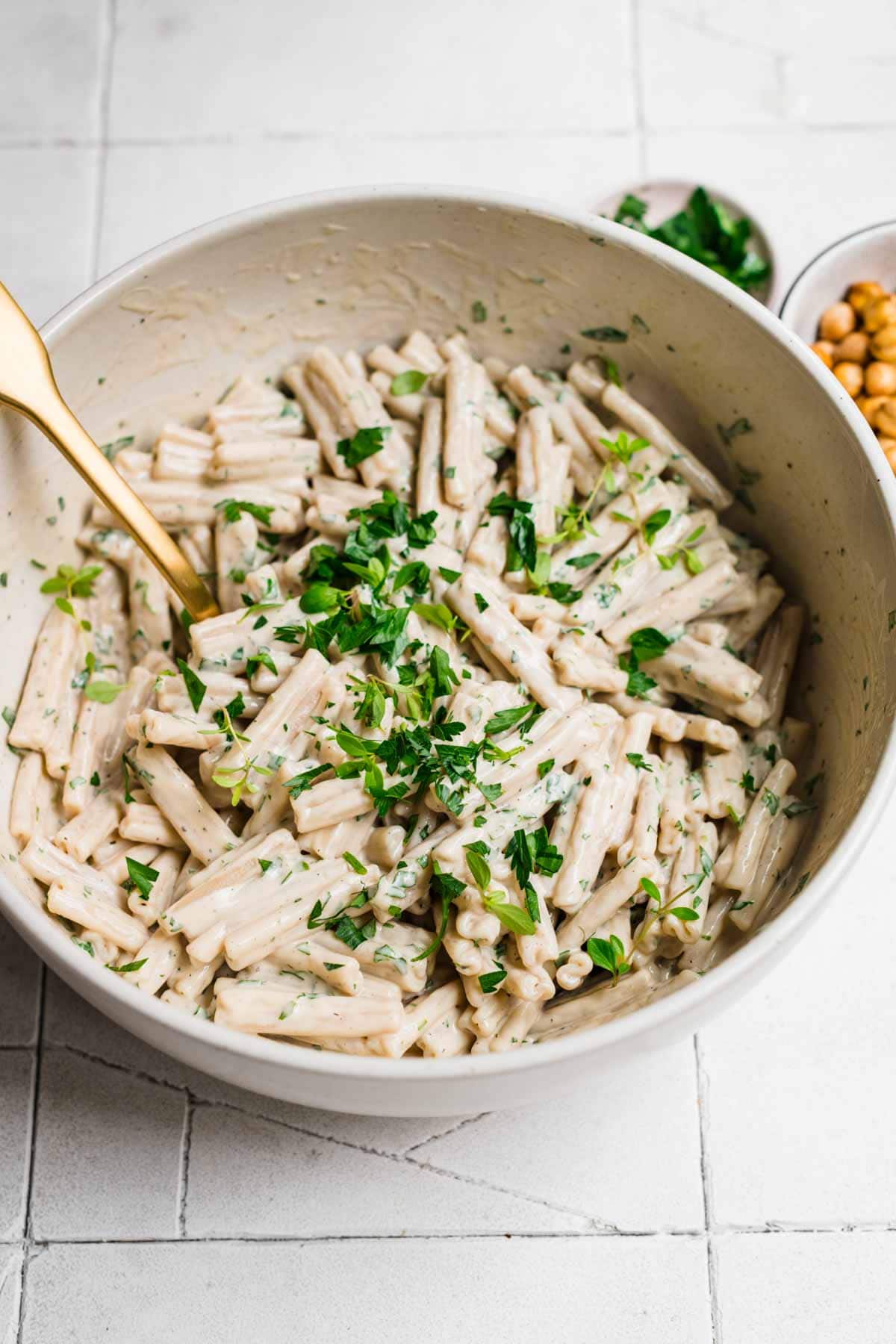 Overhead view of tahini pasta in a big mixing bowl garnished with herbs.