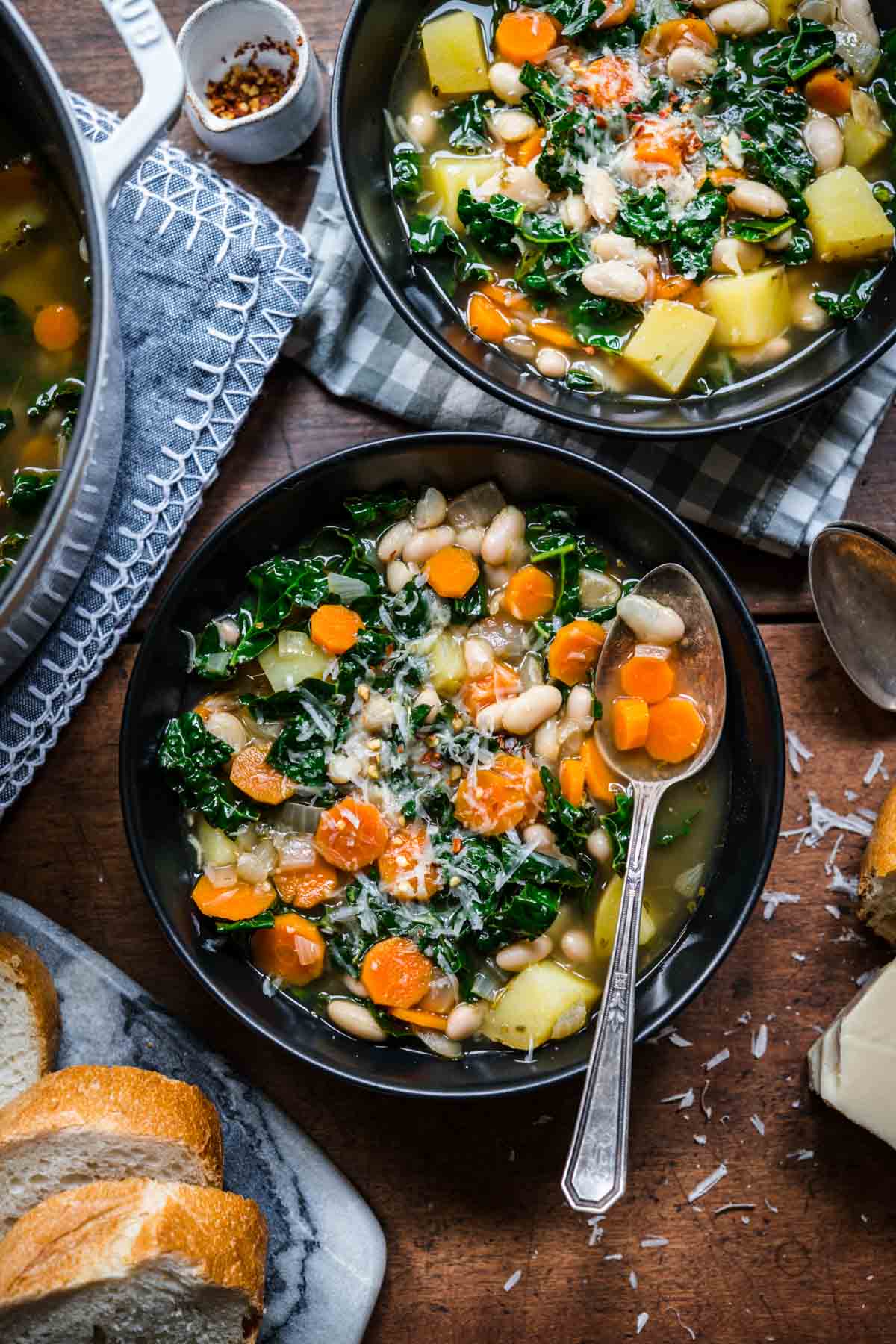 Overhead view of two bowls of white bean and kale soup with beans, carrots, and kale.