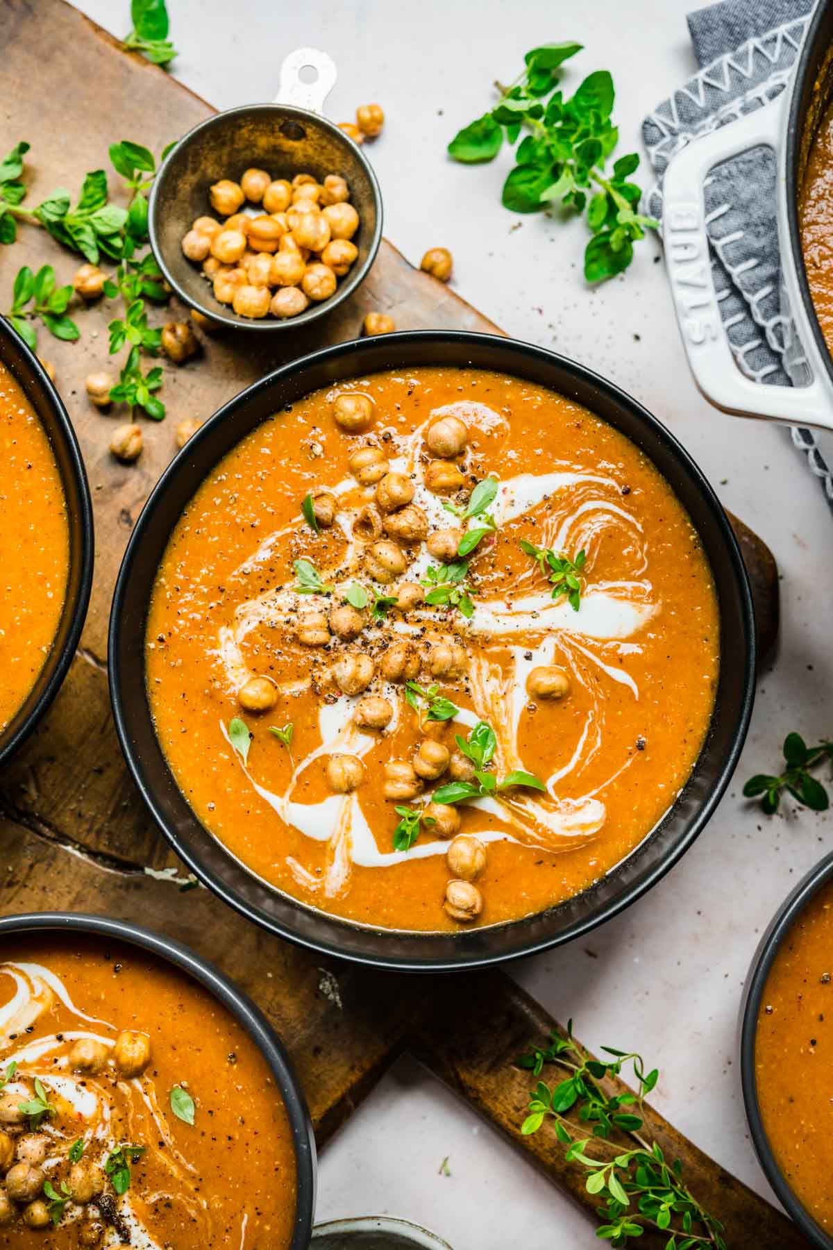 Overhead view of a bowl of red lentil soup with a garnish of chickpeas, cream, and herbs.