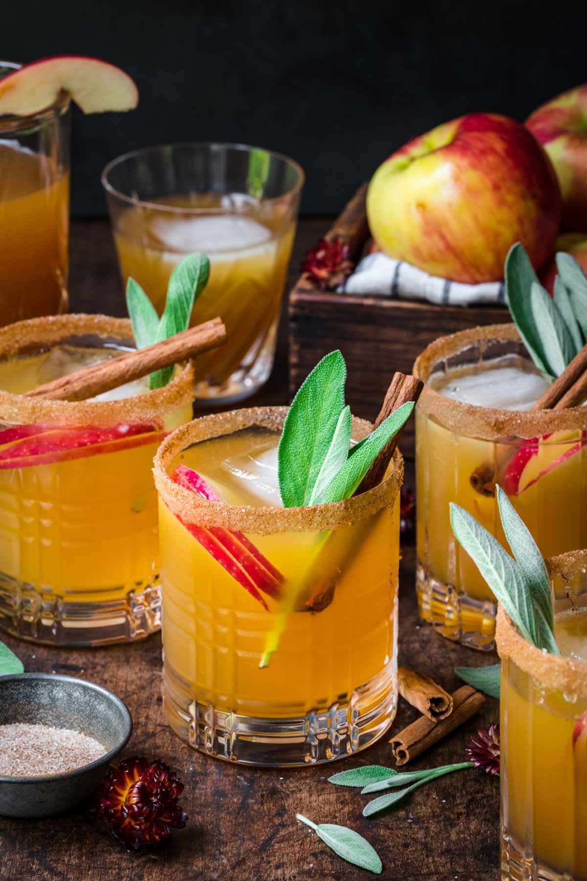 Front view of several apple cider margaritas, garnished with a cinnamon sugar rim, cinnamon stick, and herbs.