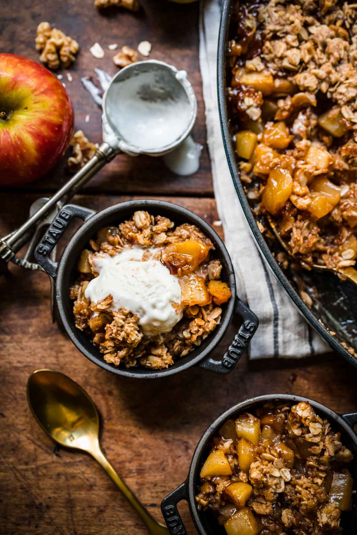 overhead view of vegan apple crisp served in mini cocottes with vanilla ice cream on top on wood table.