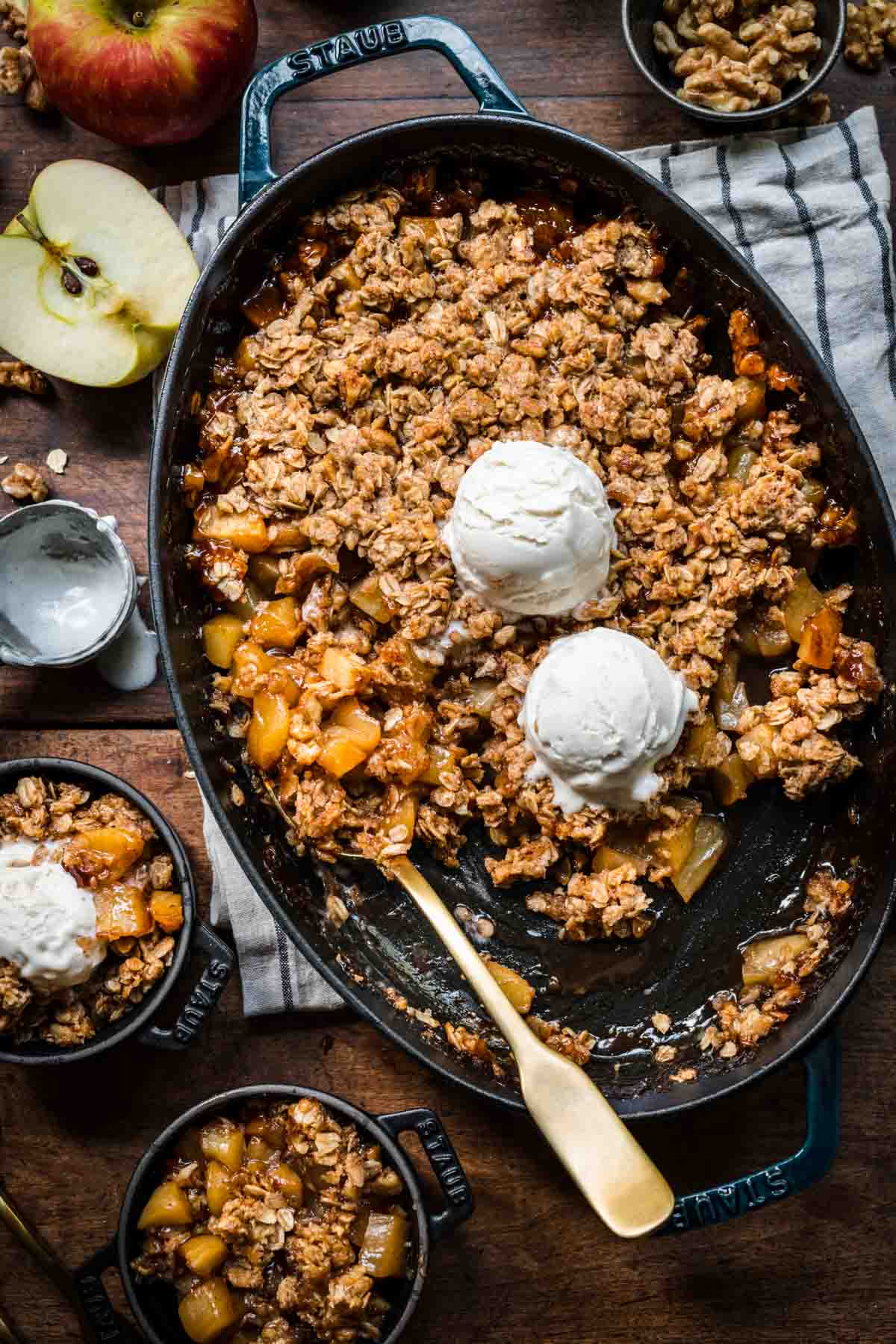 overhead view of gluten free apple crisp in an oval cast iron skillet with vanilla ice cream on top and serving spoon.