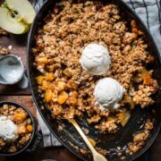 overhead view of gluten free apple crisp in an oval cast iron skillet with vanilla ice cream on top.
