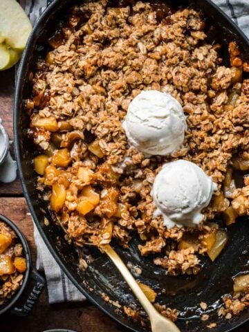 overhead view of gluten free apple crisp in an oval cast iron skillet with vanilla ice cream on top.