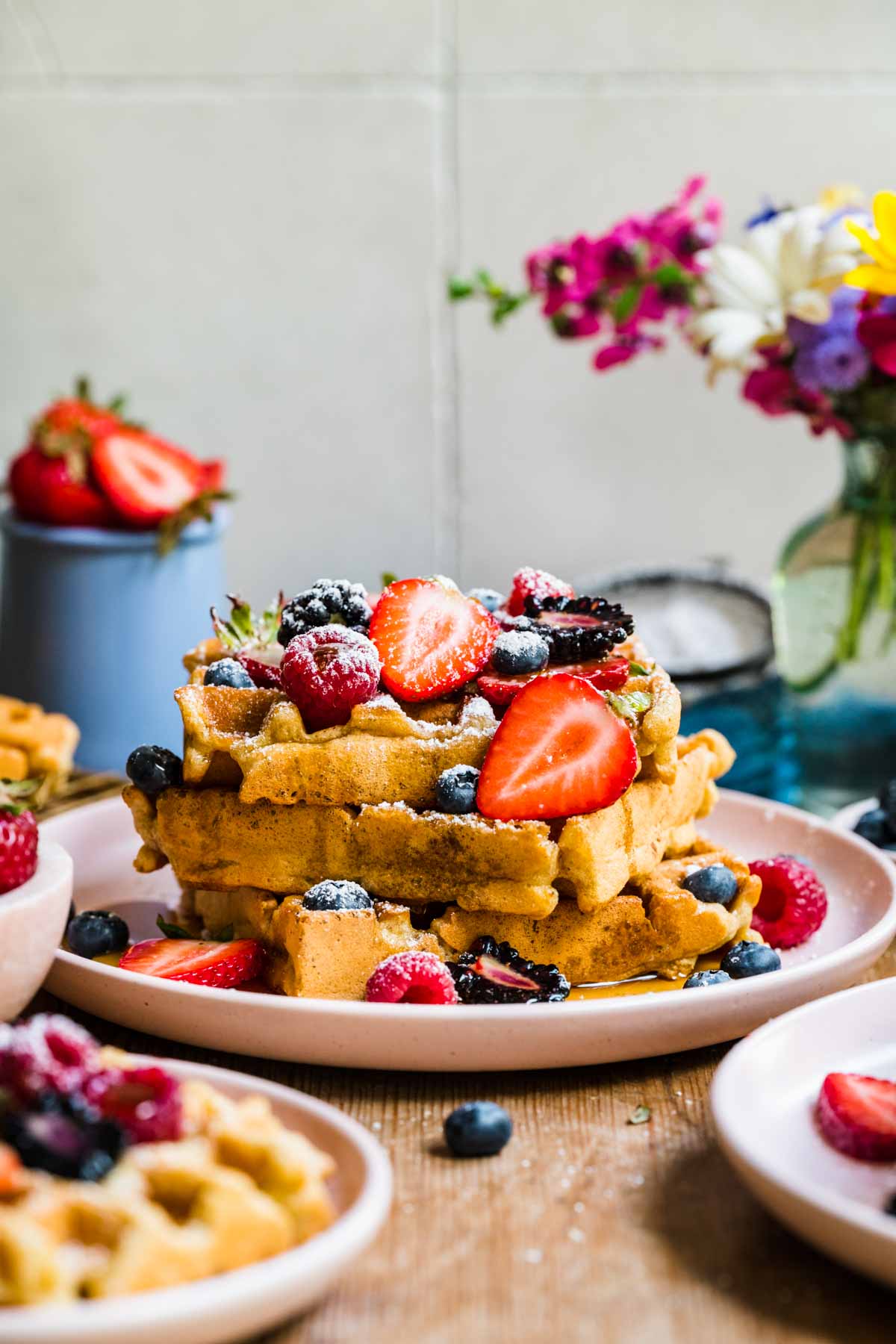 side view of a stack of vegan and gluten free waffles topped with berries, maple syrup and powdered sugar. 