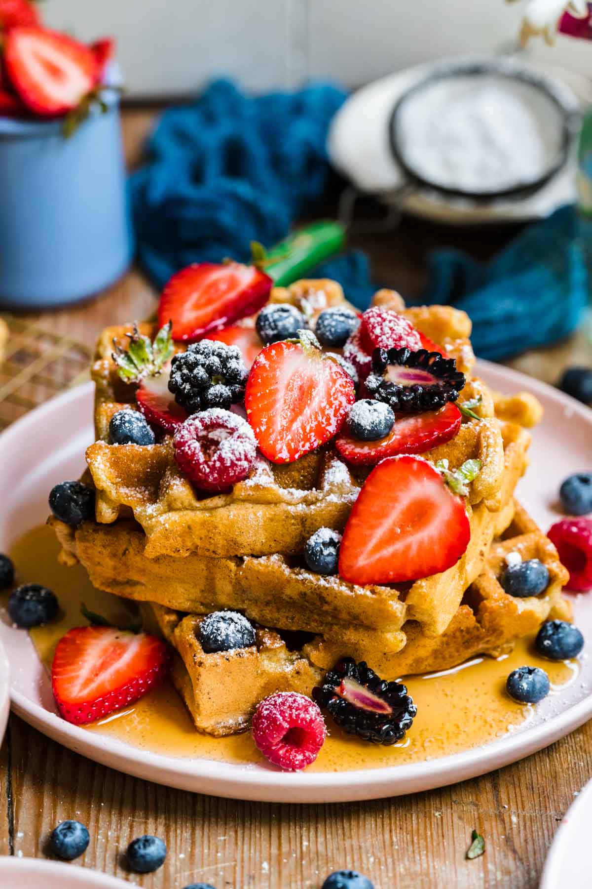 side view of a stack of vegan and gluten free waffles topped with berries, maple syrup and powdered sugar. 