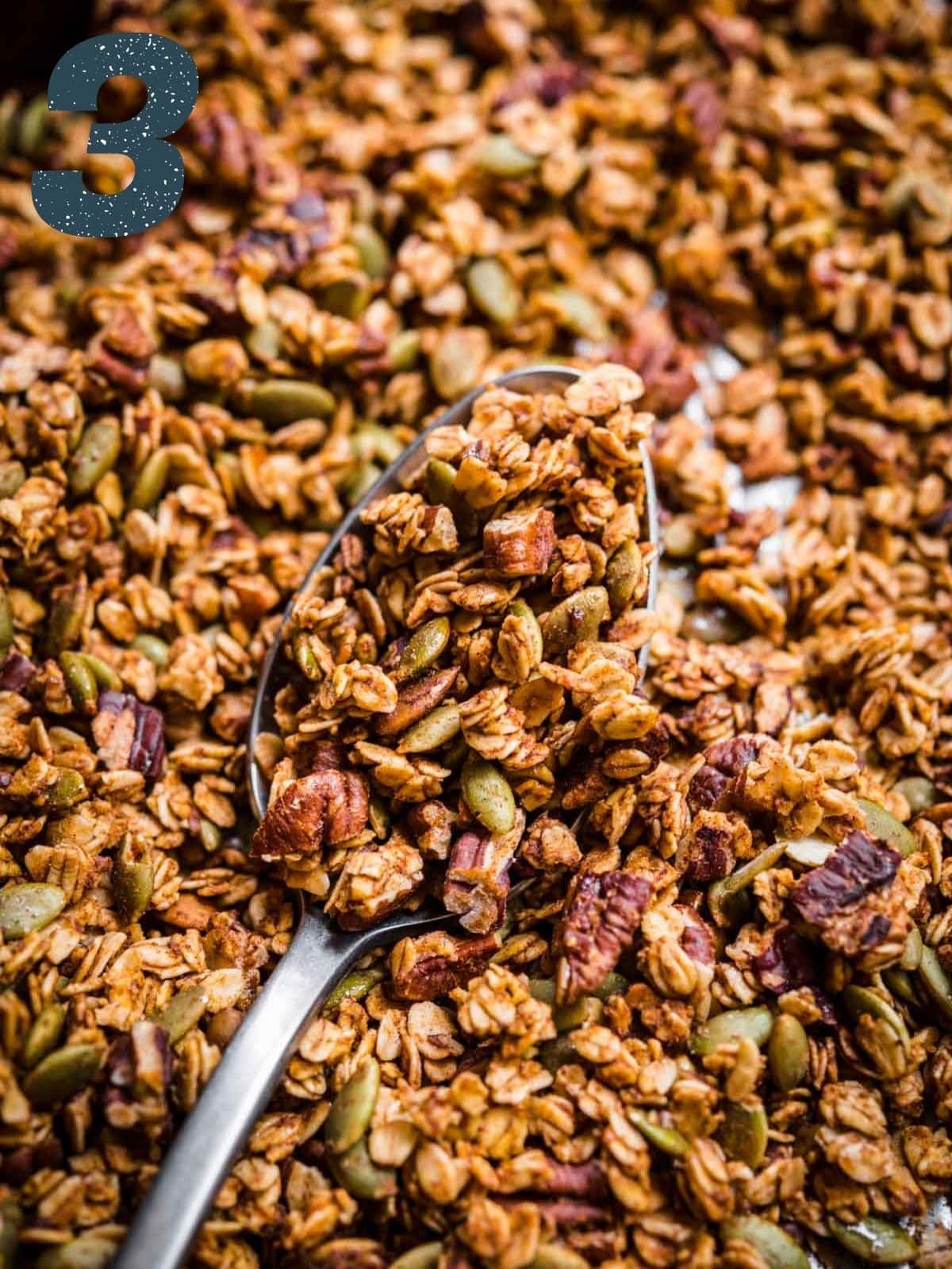 Granola on a sheet pan with some of it in a spoon facing the camera.