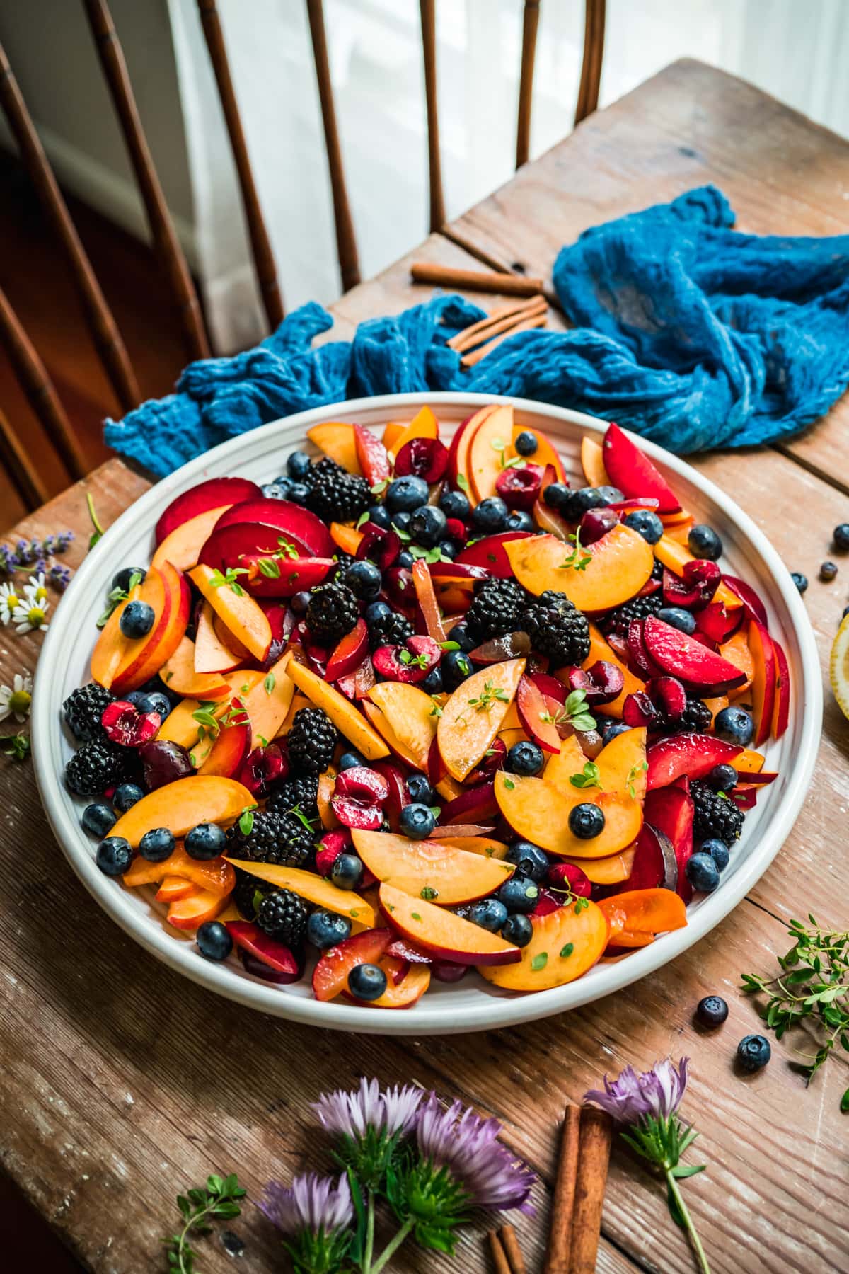 side view of summer fruit salad with stone fruit and berries on large white platter on wood table.