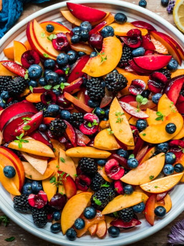 overhead view of summer fruit salad with stone fruit and berries on large white platter.