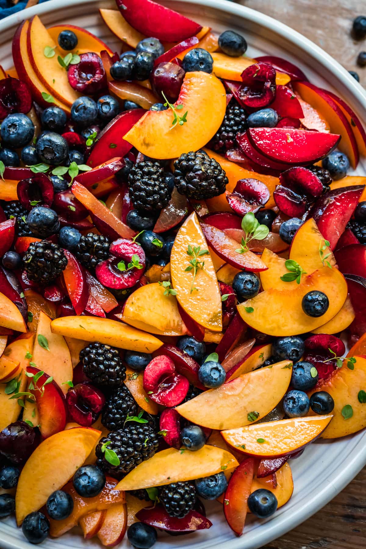 close up view of summer fruit salad with stone fruit and berries on large white platter. 