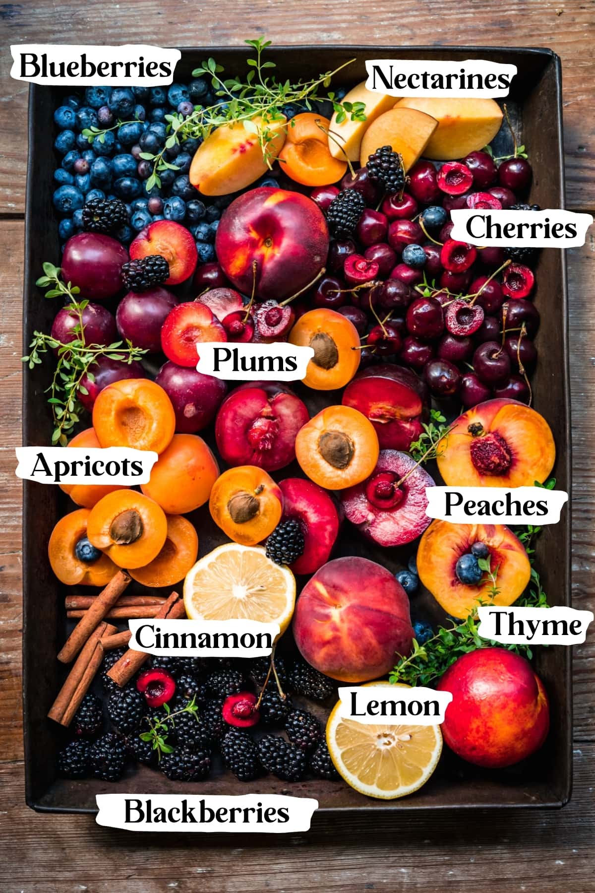 overhead view of fresh summer fruit like peaches, nectarines, cherries, blueberries, etc. on a pan. 