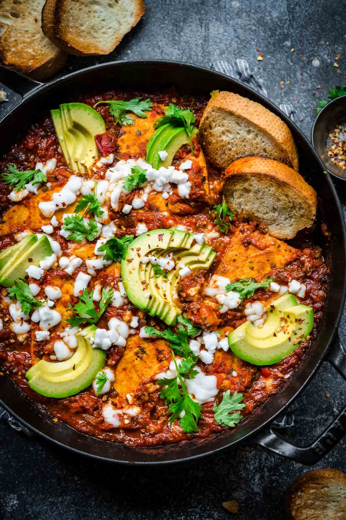 Tofu shakshuka in a cast iron skillet with parsley, vegan feta, and avocados for garnish.