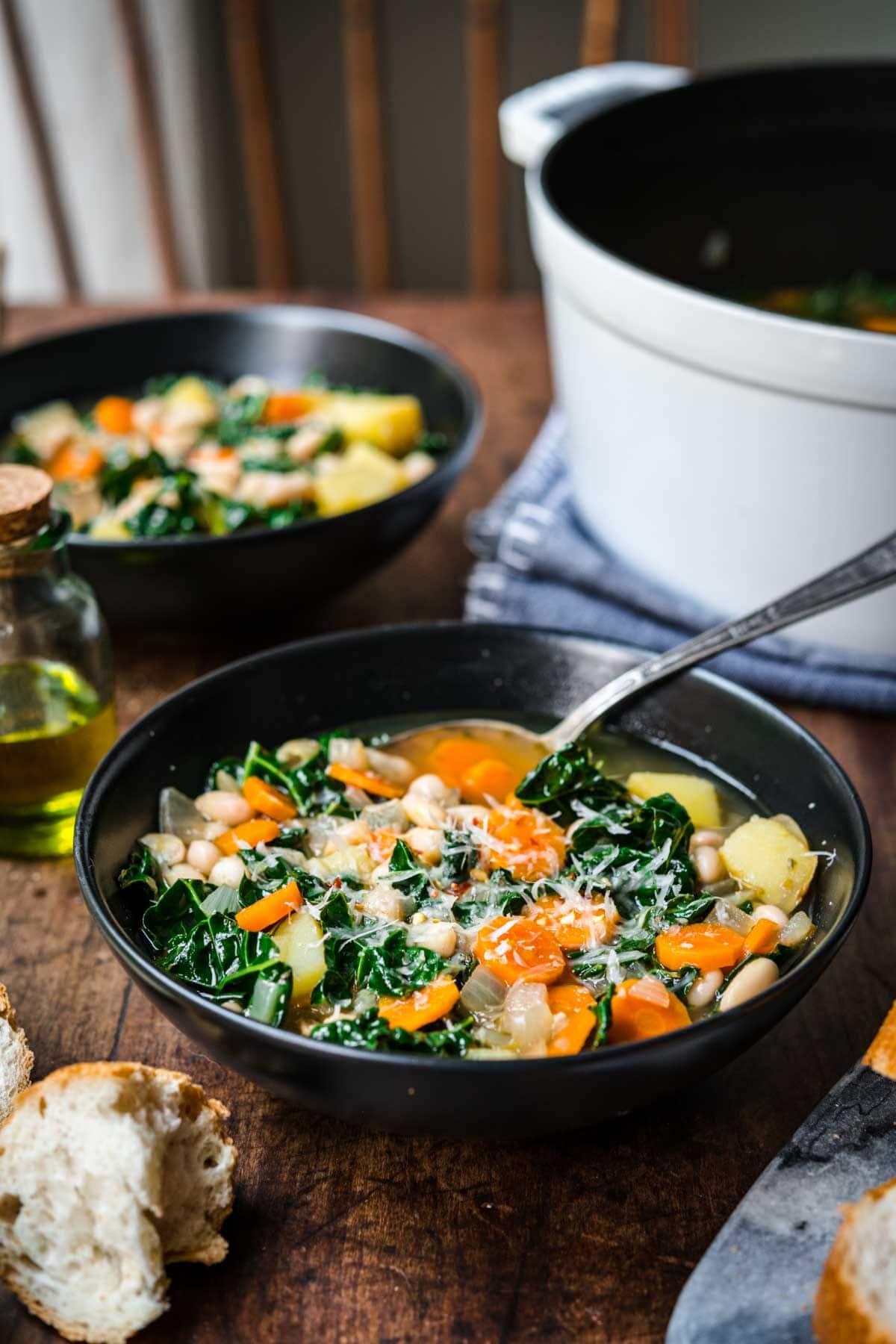 side view of white bean kale soup in black bowl on wood table. 