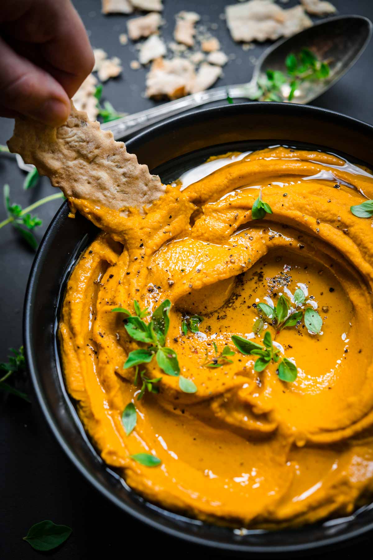 Roasted carrot dip in a bowl being scooped with a cracker.