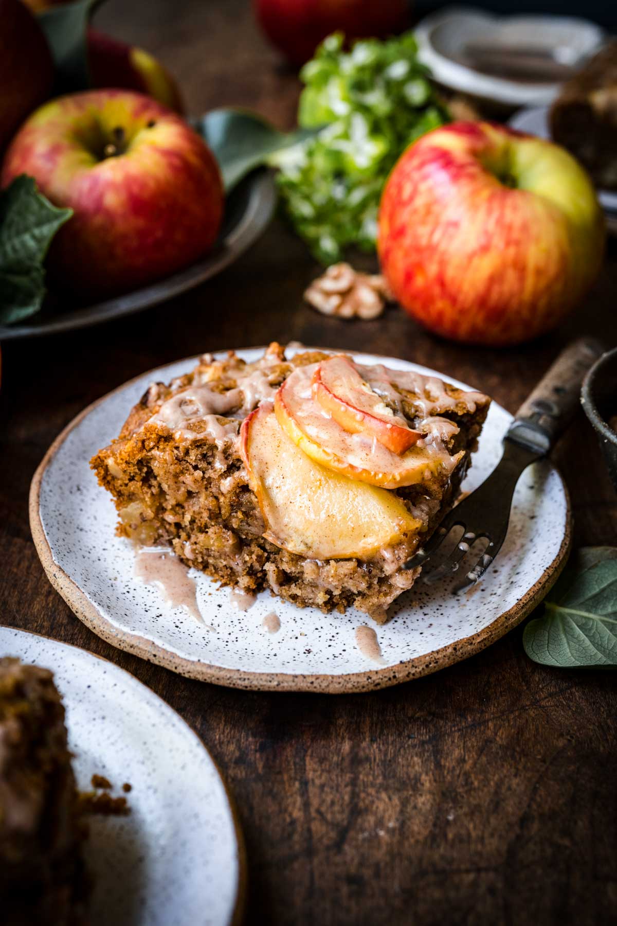 Front view of a slice of apple walnut cake on a plate with a fork.