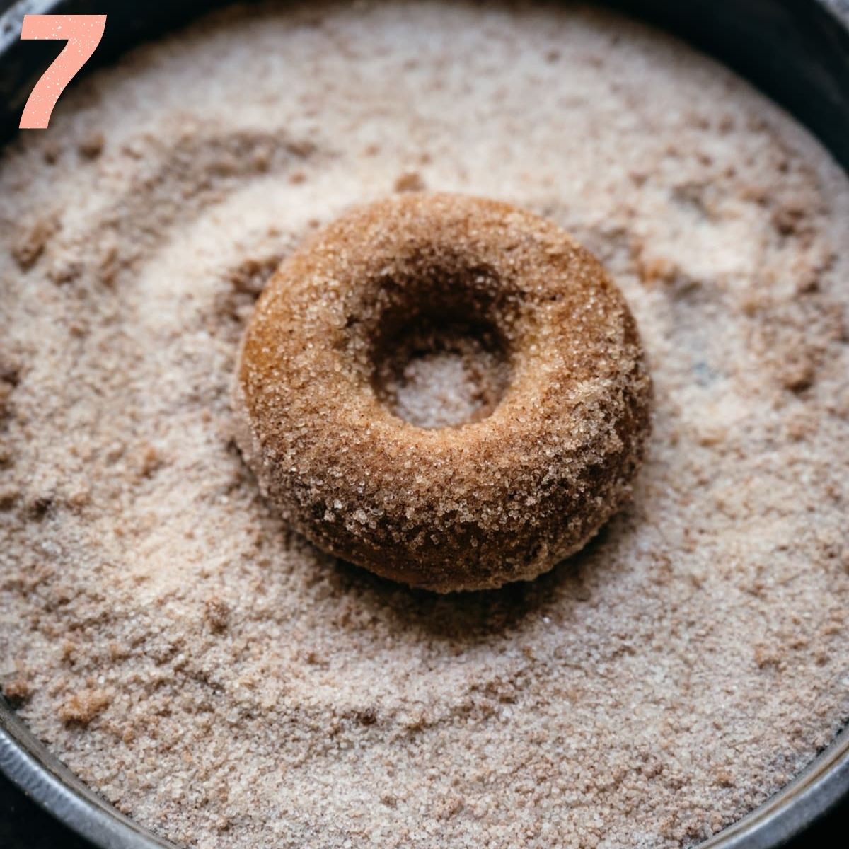 Overhead view of apple cider donut being dusted with cinnamon sugar.