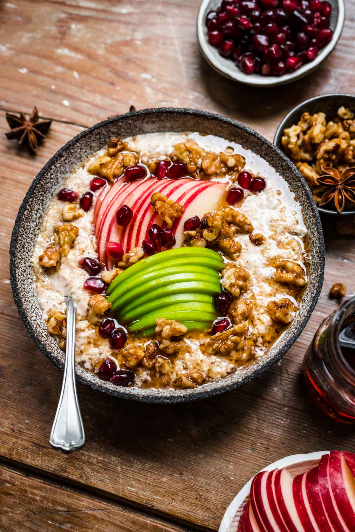 close up view of vegan apple pie overnight oats in a bowl with apple sliced, walnuts and maple syrup on wood table.