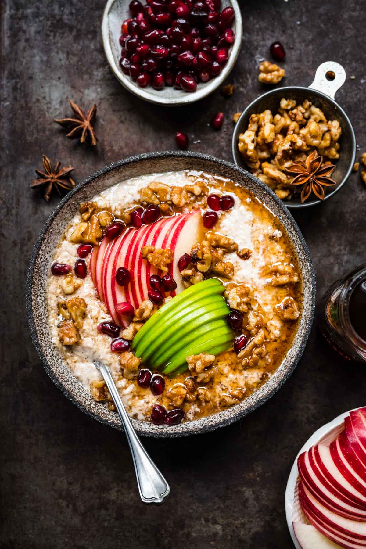 overhead view of vegan apple pie overnight oats in a bowl with apple sliced, walnuts and maple syrup on black backdrop.