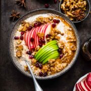 overhead view of vegan apple pie overnight oats in a bowl with apple sliced, walnuts and maple syrup on black backdrop.