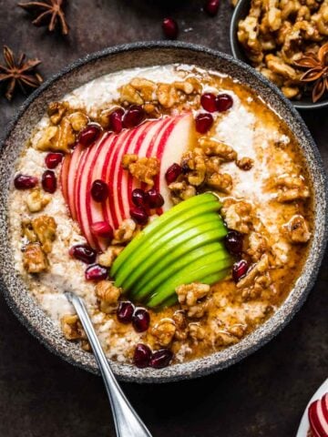 overhead view of vegan apple pie overnight oats in a bowl with apple sliced, walnuts and maple syrup on black backdrop.