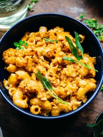 Overhead view of butternut squash mac and cheese in a blue bowl garnished with sage.