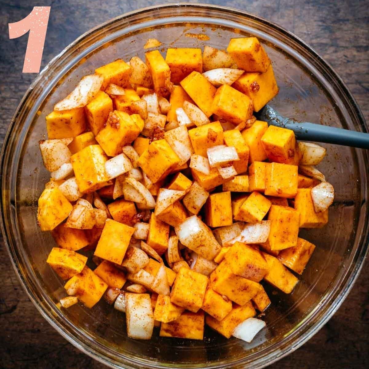 Overhead view of butternut squash and onions being stirred together with spices.