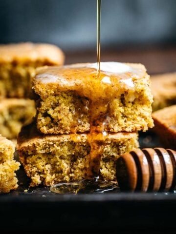 close up view of stack of gluten free vegan cornbread with drizzle of maple syrup.