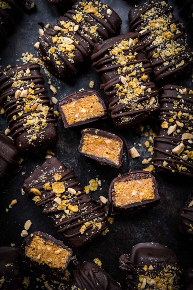 Chocolate caramel truffles with chopped nuts drizzled on top, close-up shot on a dark surface.