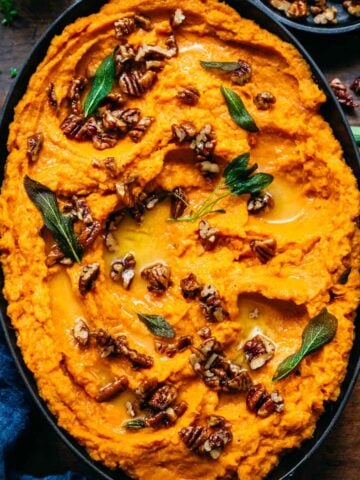 Overhead view of mashed sweet potatoes garnished with nuts and herbs.