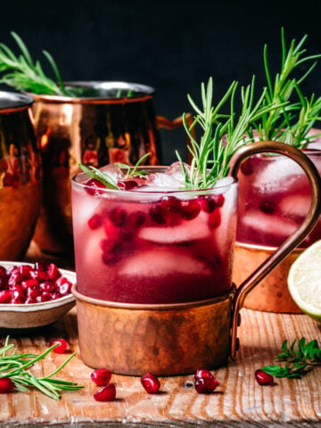 side view of pomegranate moscow mule in copper cocktail glass on wood table.