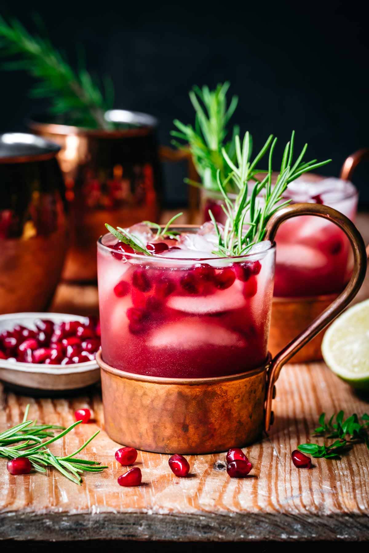 side view of pomegranate moscow mule in copper cocktail glass on wood table. 