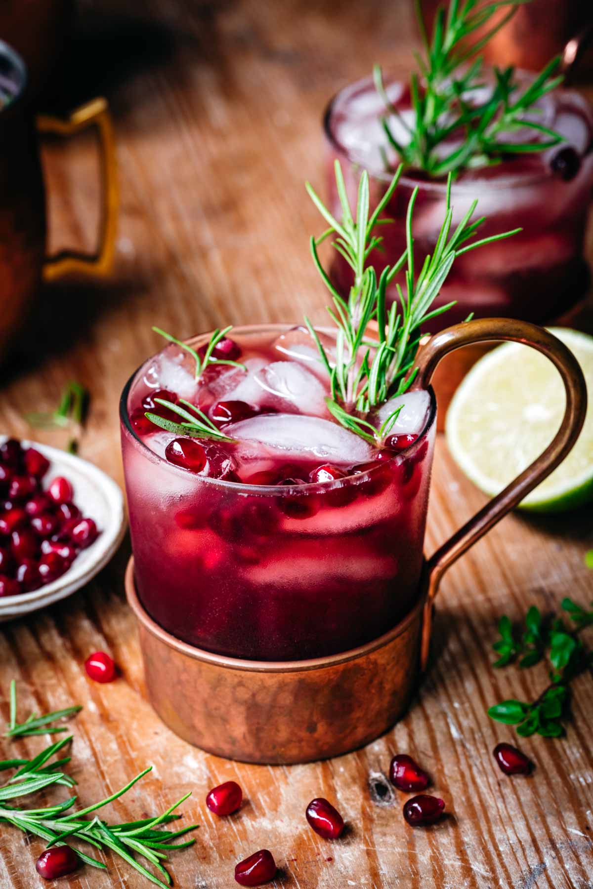 side view of pomegranate moscow mule in copper cocktail glass on wood table. 