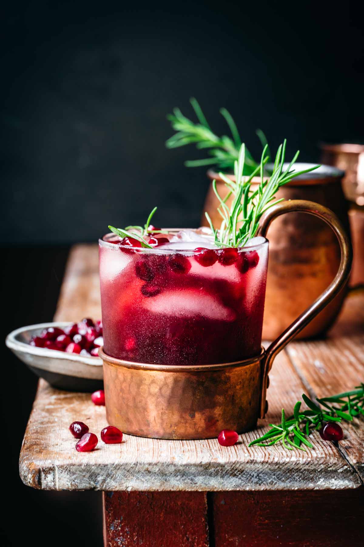 side view of pomegranate moscow mule in copper cocktail glass on wood table. 