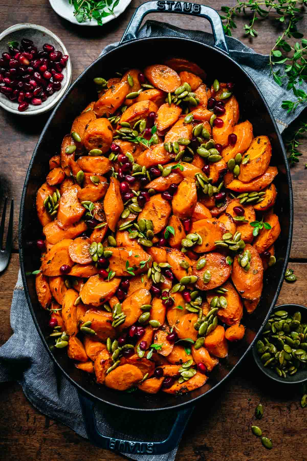 Overhead view of glazed carrots in a pan with pomegranate and pumpkin seeds.