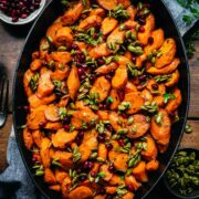 Close up view of maple glazed carrots in a pan garnished with pumpkin seeds and pomegranate.