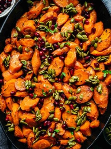 Close up view of maple glazed carrots in a pan garnished with pumpkin seeds and pomegranate.