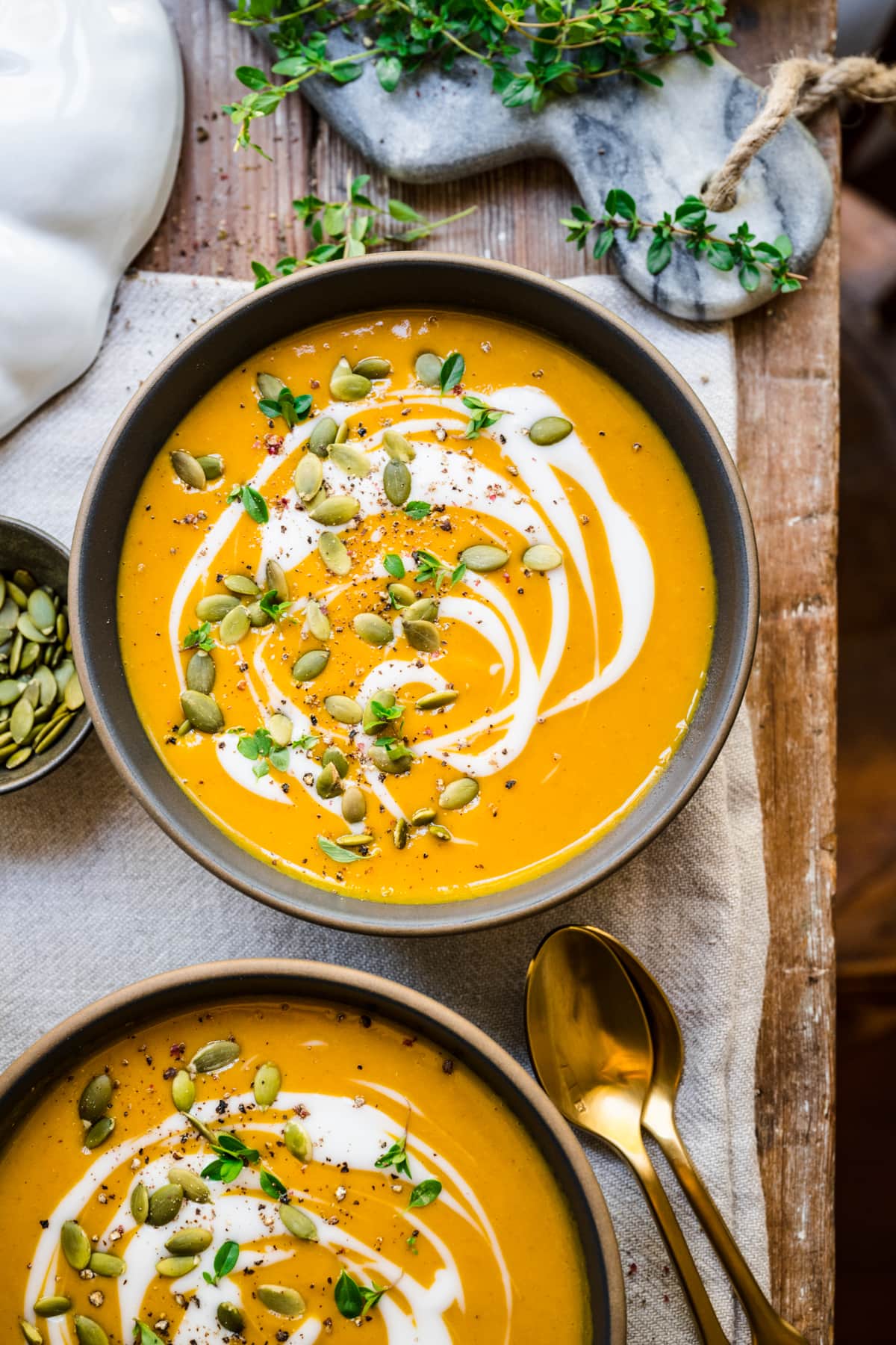 Overhead view of pumpkin soup with swirls of cream and pumpkin seeds on top.