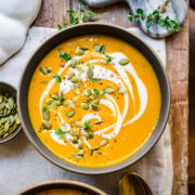 Overhead view of pumpkin soup garnished with a swirl of cream and pumpkin seeds.