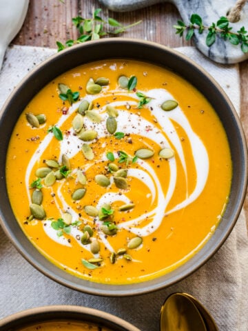 Overhead view of pumpkin soup garnished with a swirl of cream and pumpkin seeds.