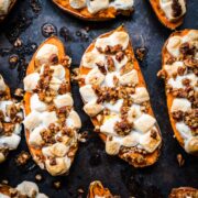 close up view of twice baked sweet potatoes topped with mini marshmallows and pecans on sheet pan.