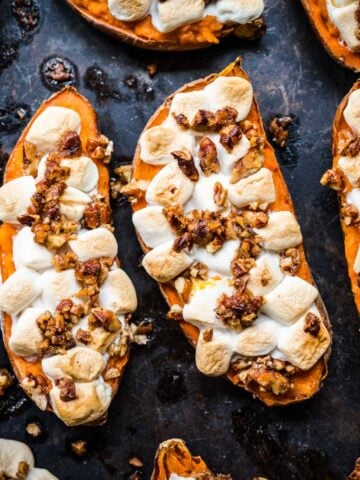 close up view of twice baked sweet potatoes topped with mini marshmallows and pecans on sheet pan.