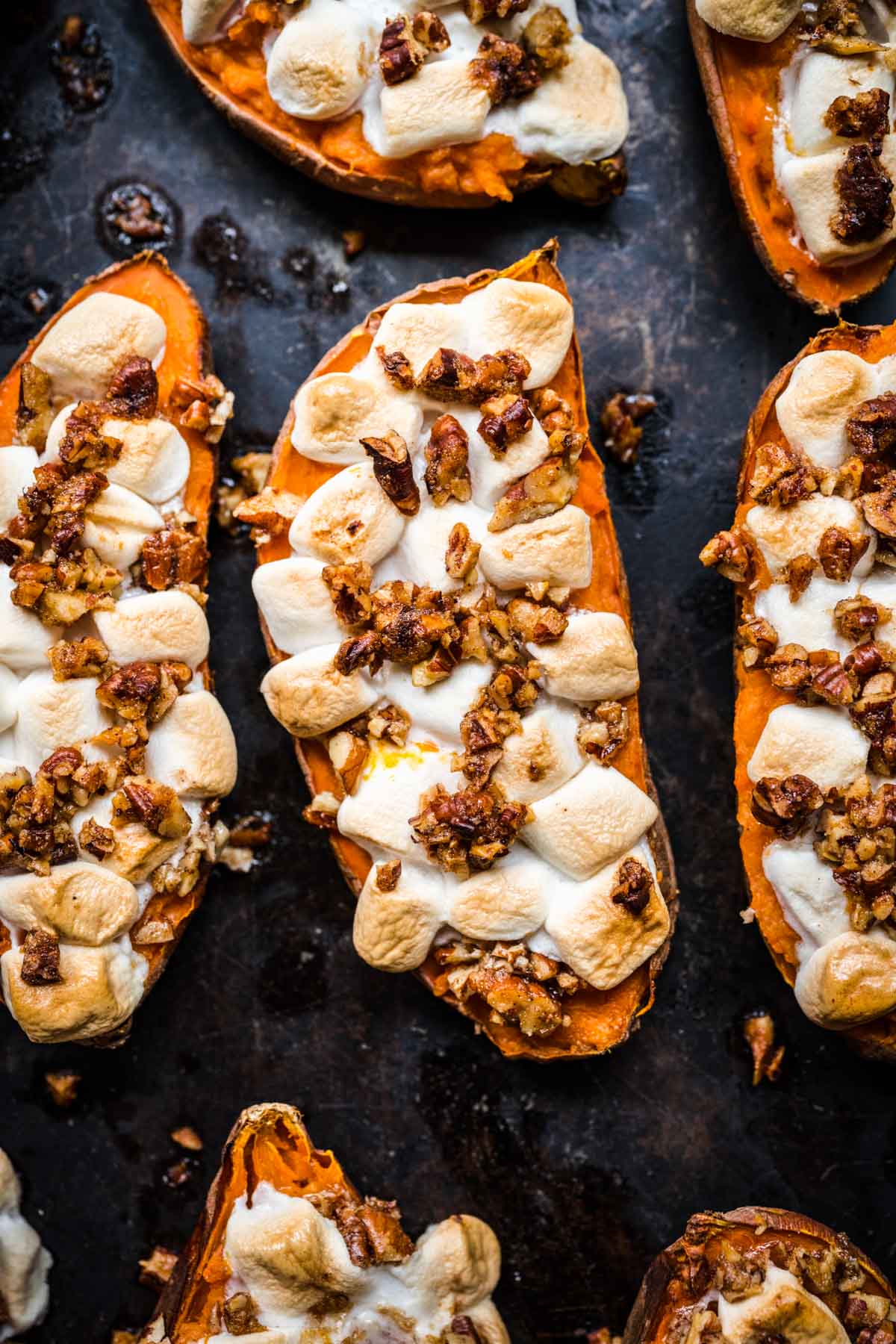 close up view of twice baked sweet potatoes topped with mini marshmallows and pecans on sheet pan. 