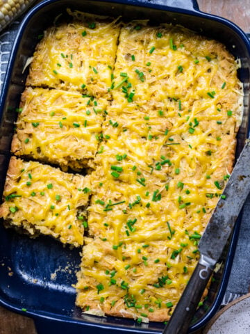 Overhead view of corn casserole in a baking dish topped with cheese and chives.