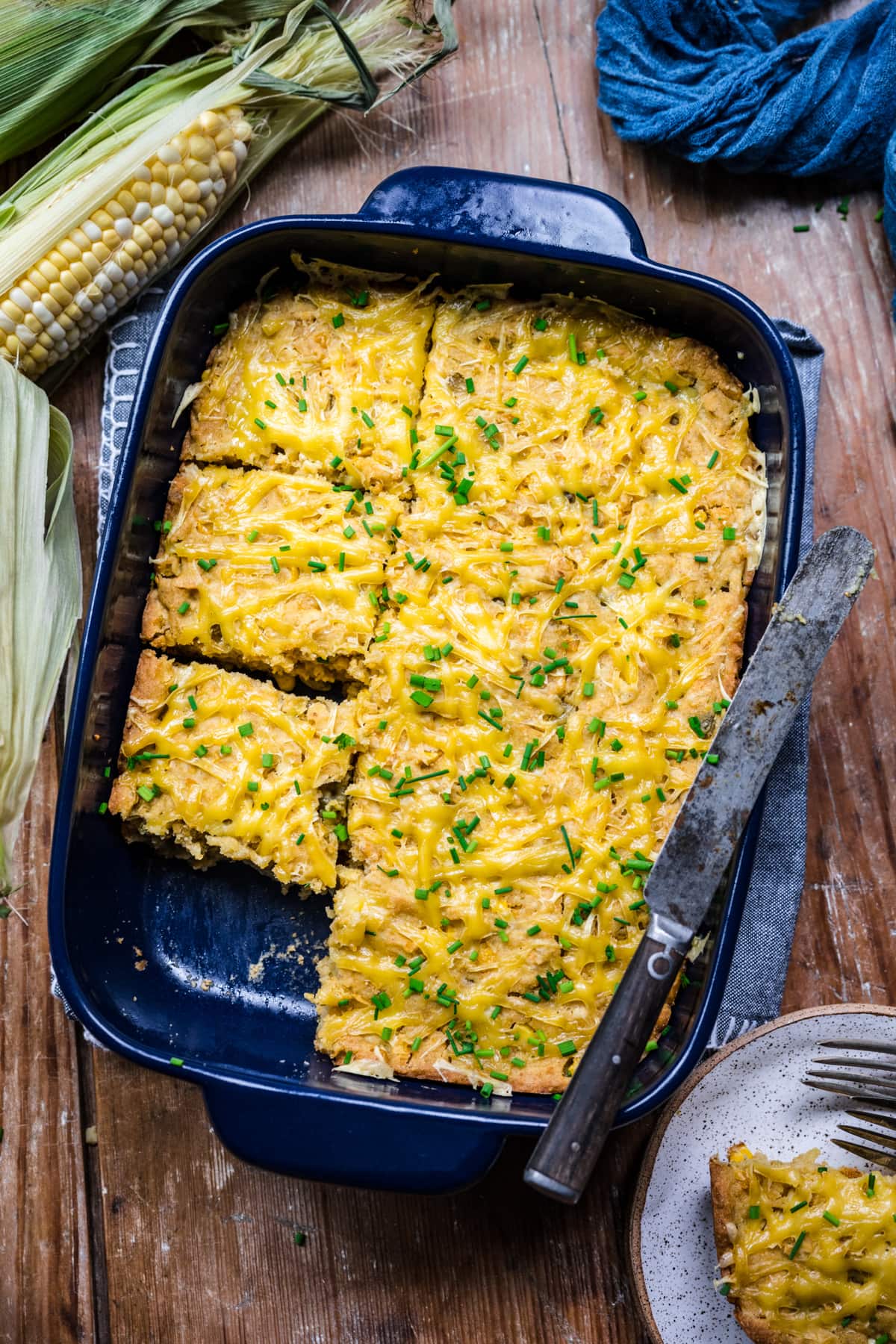 Overhead view of corn casserole in a blue baking dish with a spatula on top.